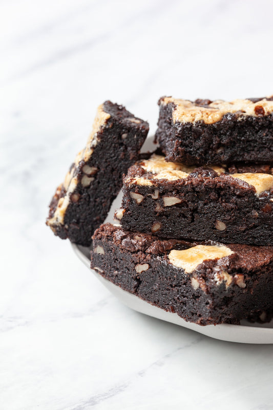 4 Rocky Road Brownies on a white plate- We've reimagined the nostalgic ice cream flavor and these special treats feature signature WGD brownie batter studded with premium walnuts, crowned with gooey semi-melted marshmallows and chocolate chips.