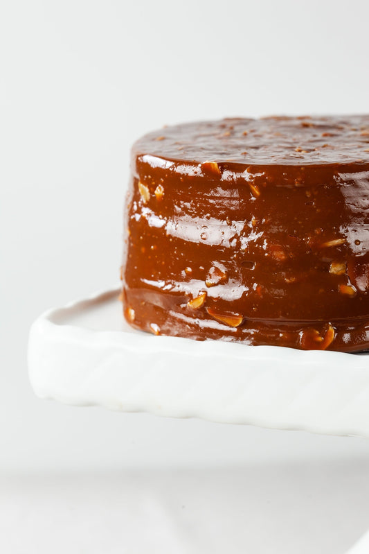 A whole Southern-style Caramel Cake featuring rich butterscotch icing, toasted almonds, and yellow cake layers on a white cake platter from William Greenberg Desserts.