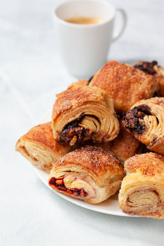 Assorted William Greenberg Desserts freshly baked Rugelach on a white plate with coffee in a cup in the background. behind