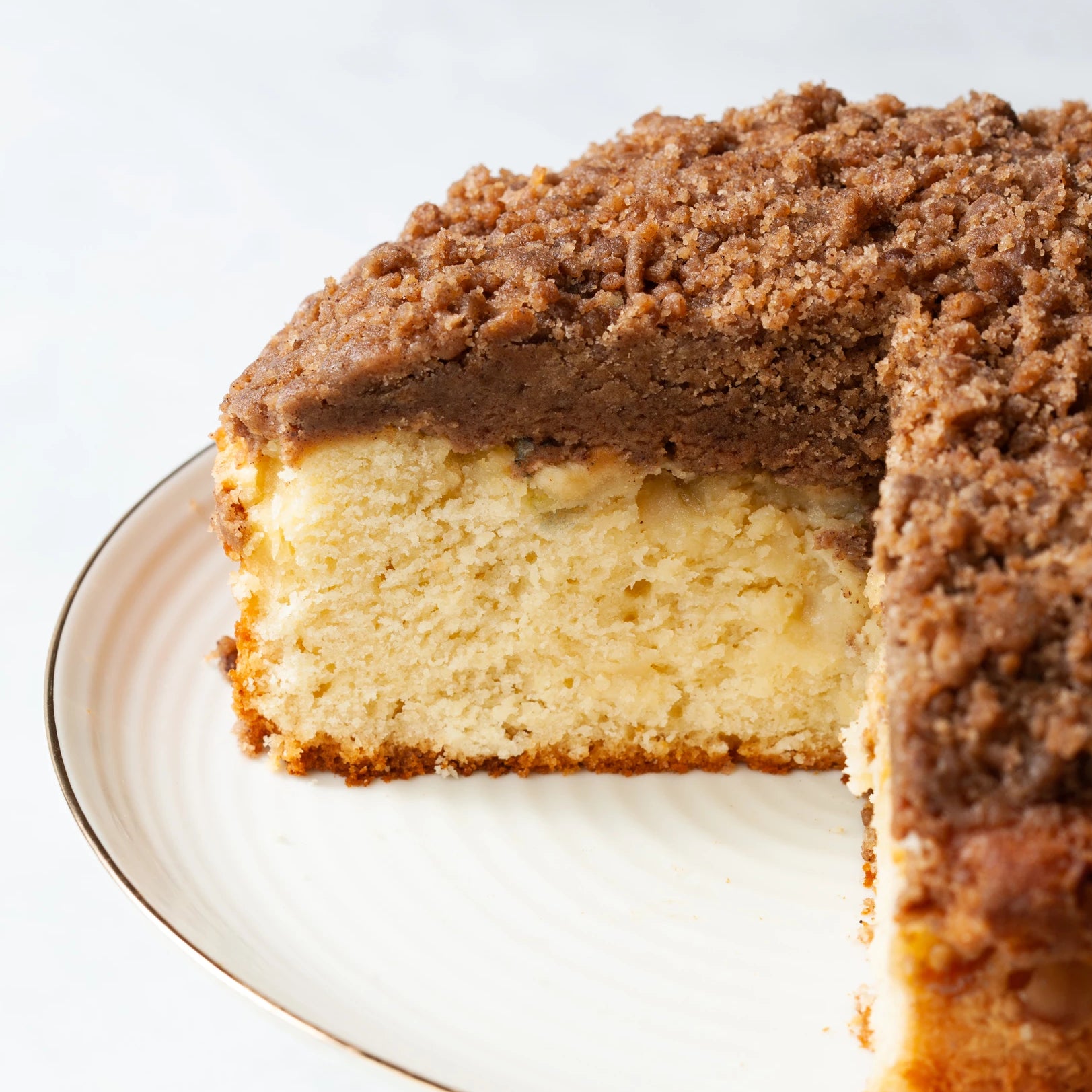 An apple strusel butter cake on a white plate with a piece removed.