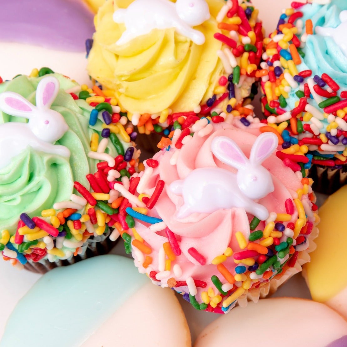 Easter cupcakes with bunnies on them from William Greenberg Desserts, surrounded by pastel black and white cookies.