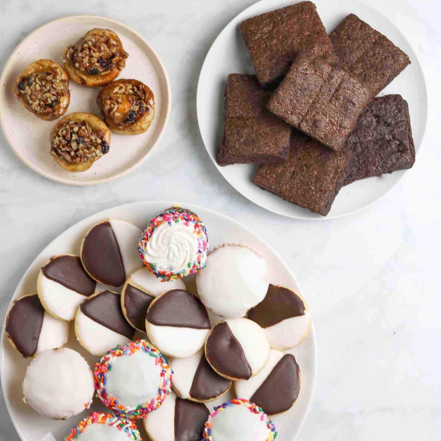 An overhead shot of 6 brownies on a plate, black & white cookies, white frosted cupcakes on a plate and 4 schnecken on another plate from William Greenberg Desserts. Called the New York Strong Box 