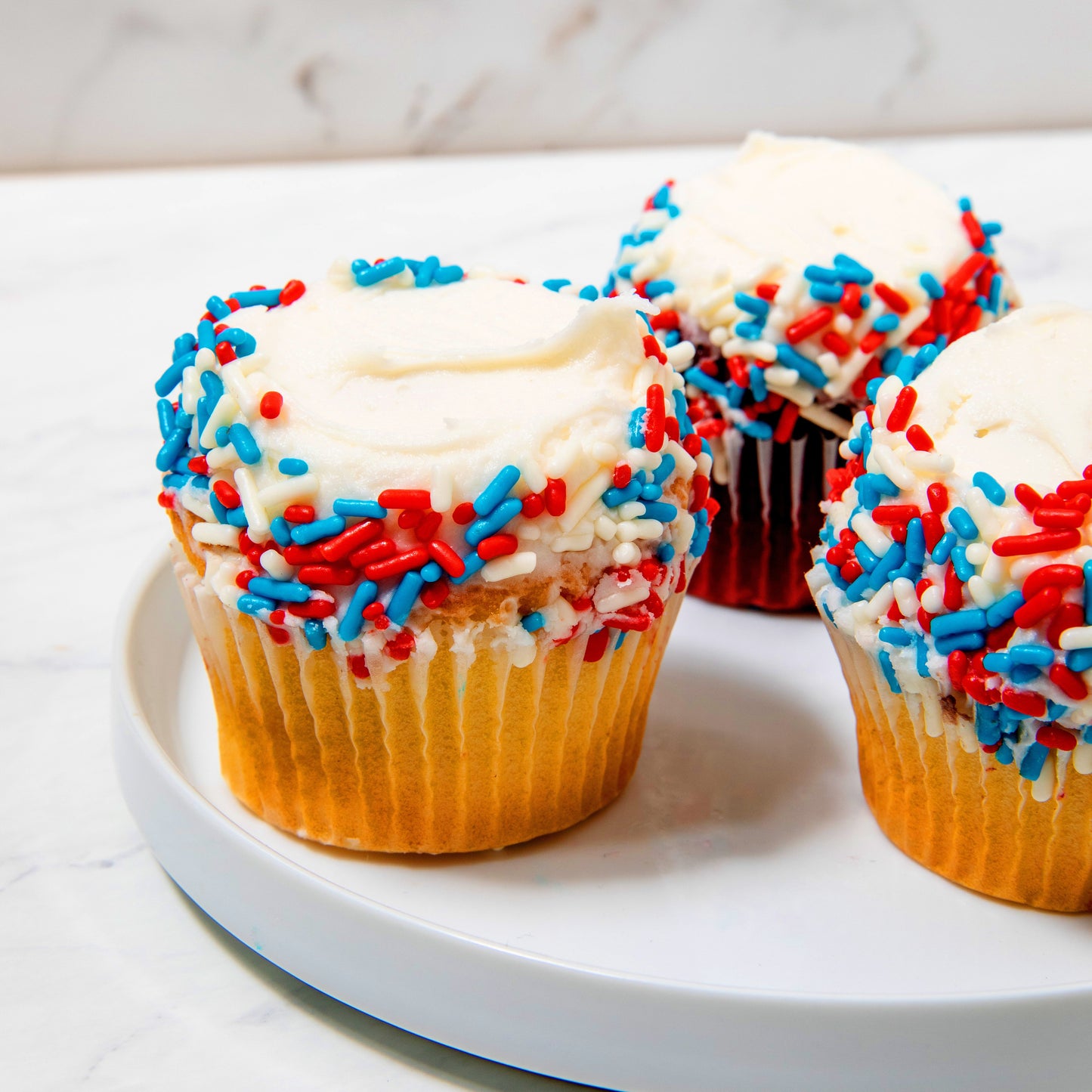 Three vanilla buttercream iced cupcakes decorated with red, white and blue sprinkle.