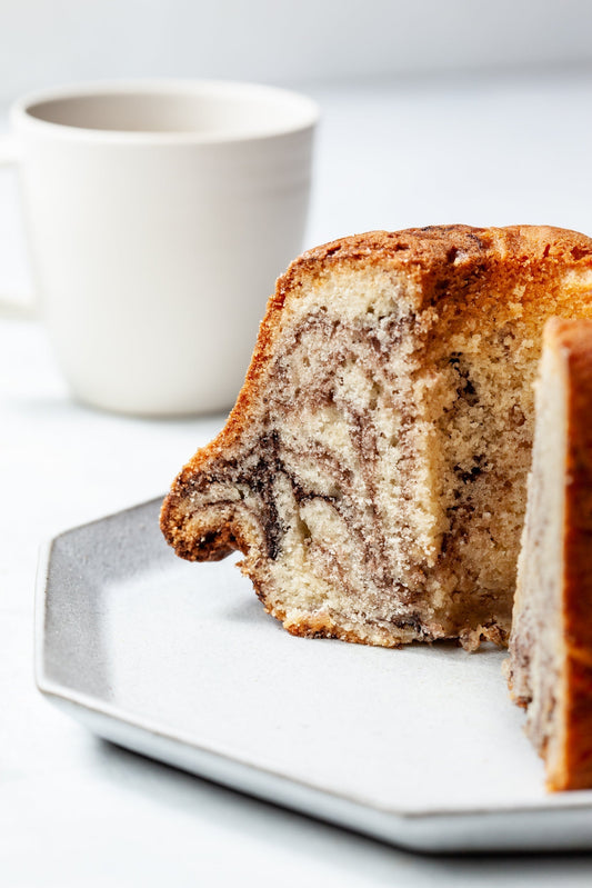 A william greenberg marble coffee cake with a slice taken out to show the chcolate marbling and a coffee cup in the background.
