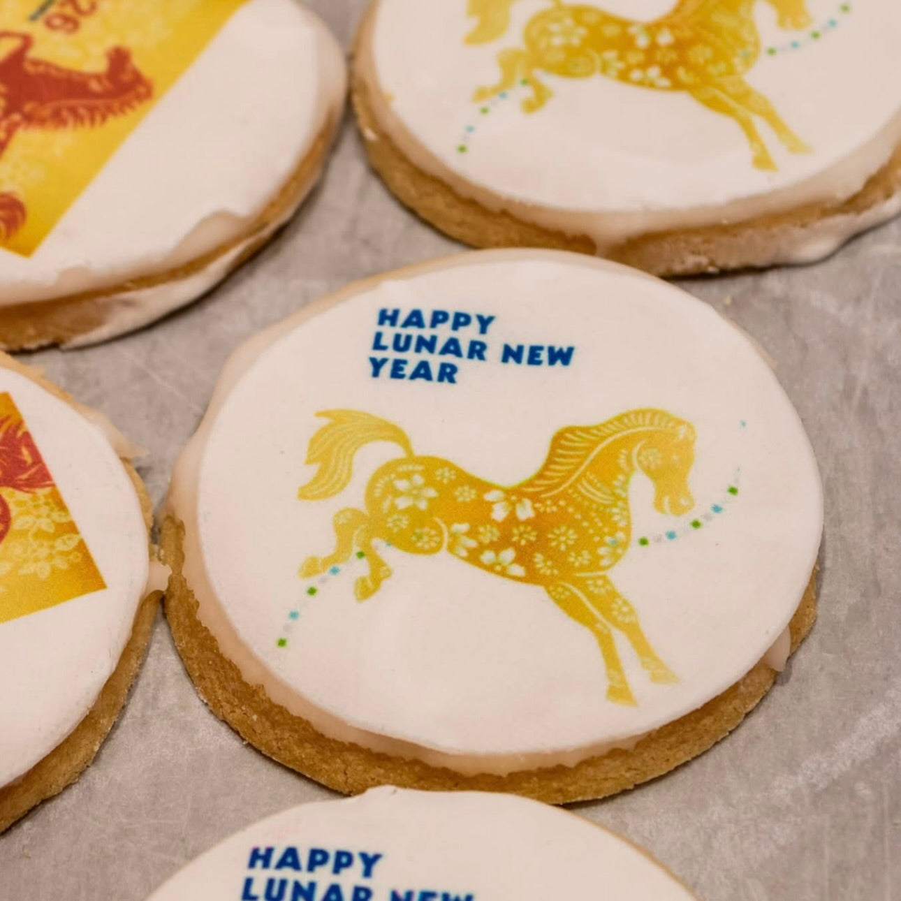 Cookies with gold horse designs and 'Happy Lunar New Year' text on a gray surface