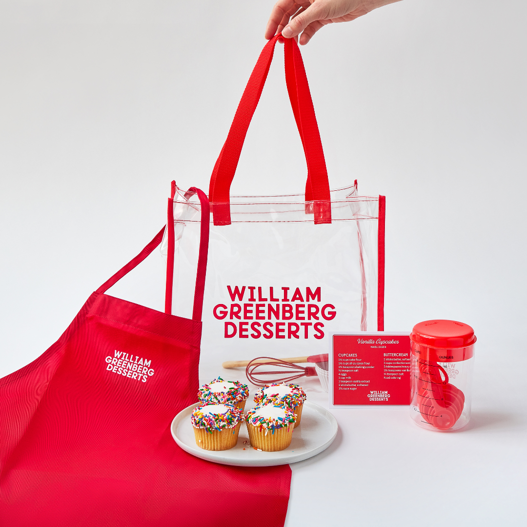 William Greenberg Desserts kids baking kit featuring an apron, recipes, 4 cupcakes, measuring spoons, a whisk and a mixing spoon.