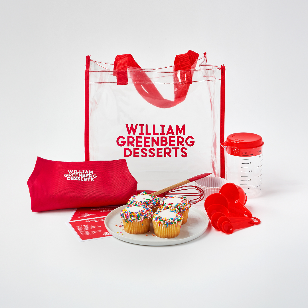 William Greenberg Desserts kids baking kit featuring an apron, recipes, 4 cupcakes, measuring spoons, a whisk and a mixing spoon.