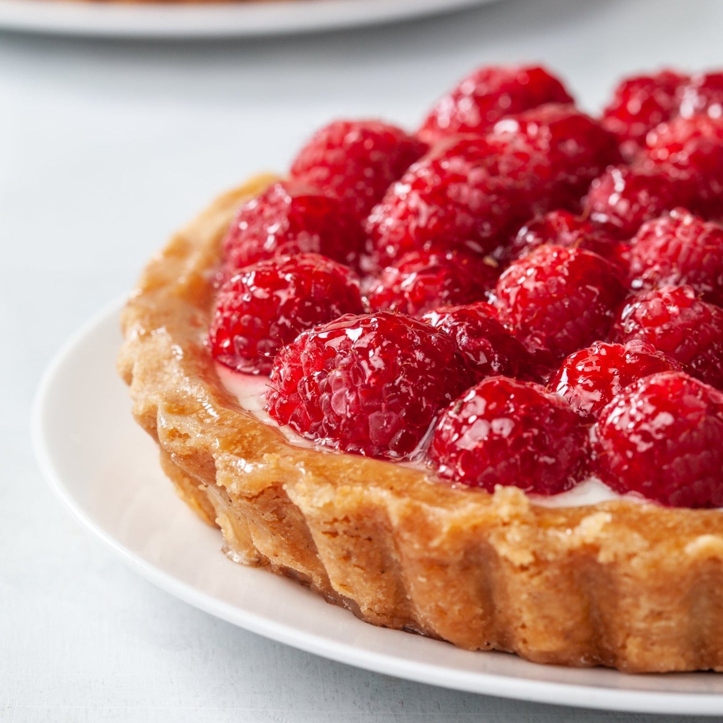 Raspberry tart with crimped edges on a white plate