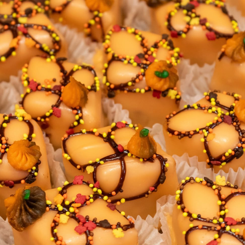 Decorative petit fours decorated with pumpkins with colorful toppings in little paper pastry cups.