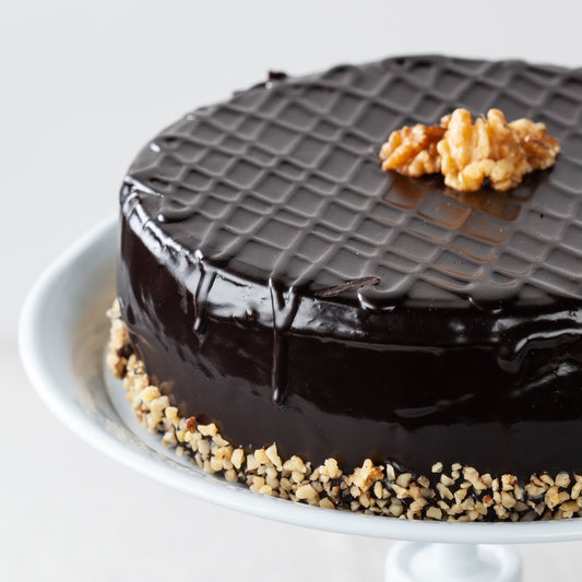 A chocolate iced walnut cake on a cake stand.