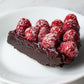 A slice of dense chocolate cake topped with raspberries and dusted with powdered sugar