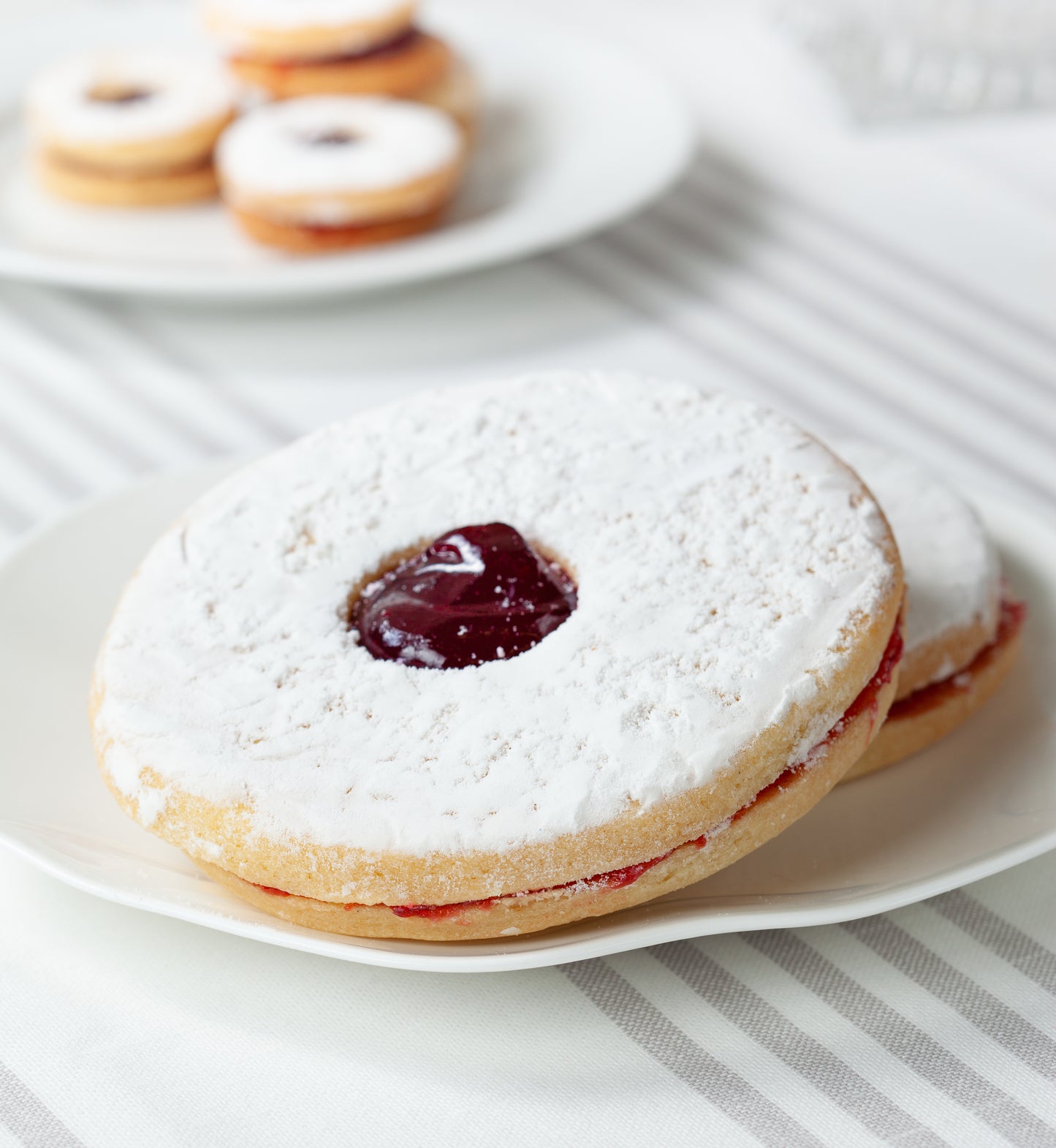 Large and smal Linzer tarts filled with raspberry jam on plates on a striped table cloth